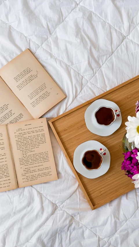 two cups of coffee and a book on the bed