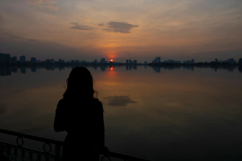 a person standing on a balcony watching the sunset over the water