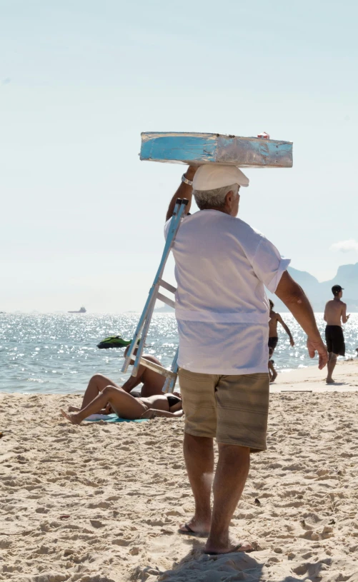 man on the beach carrying a surf board on his head