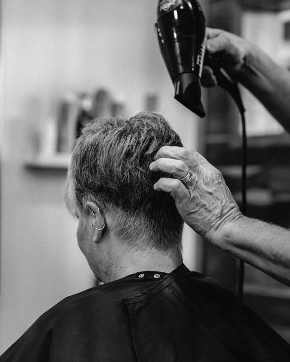 black and white pograph of a man getting his hair styled by an old person