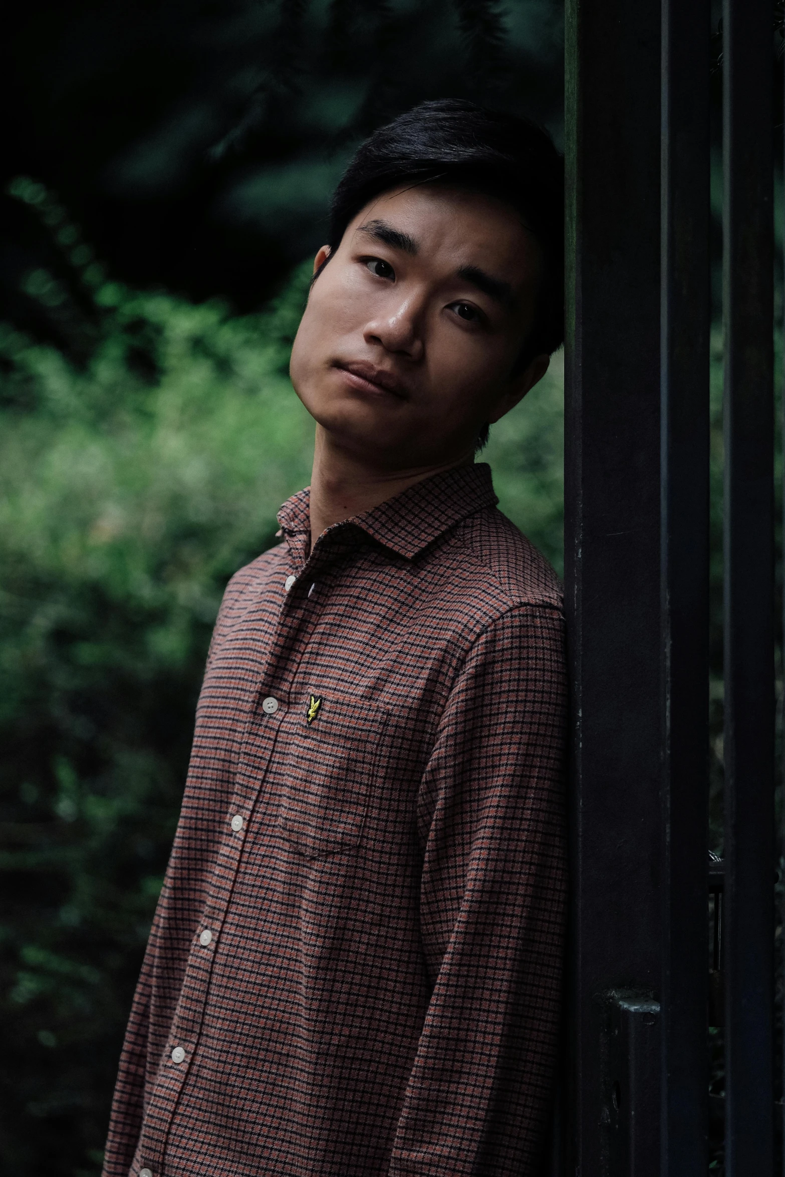 a man leans against the wall in his red checked shirt