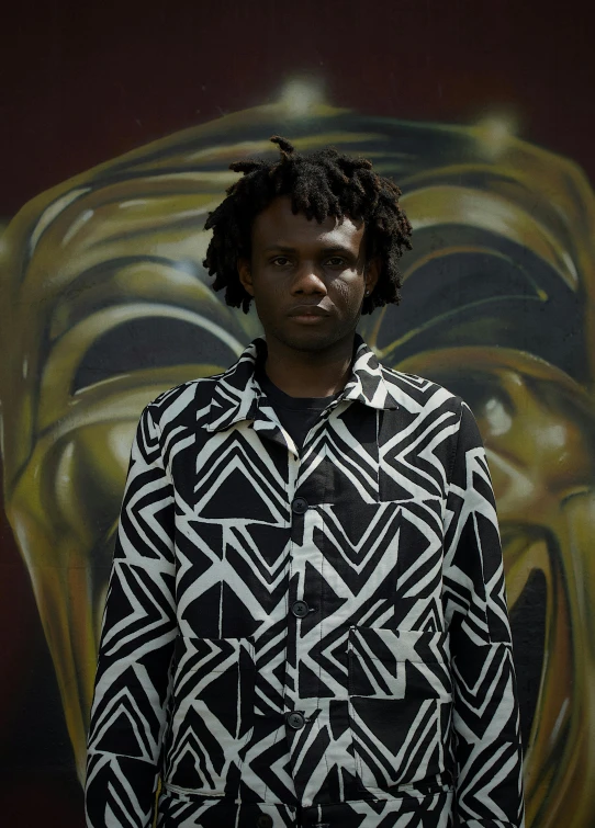 a man in a black and white shirt standing next to a painting of a face