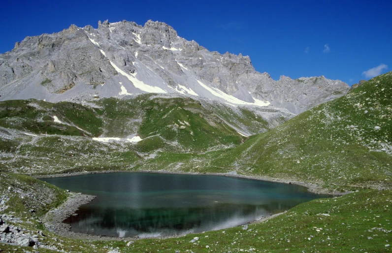 a lake surrounded by mountains on the edge of the grass