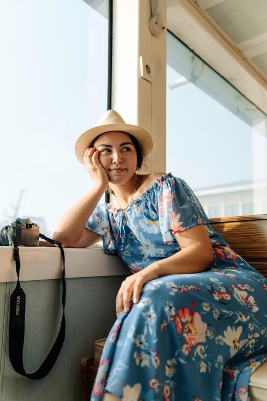 woman wearing hat and dress sitting on bench near window