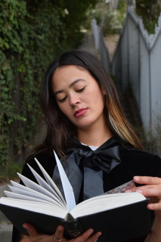 a woman reading an open book in front of trees