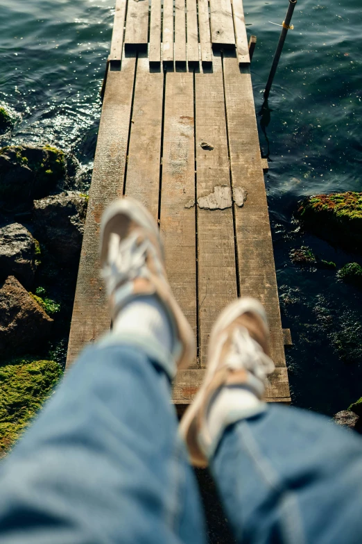 a person in blue jeans and shoes is looking at the water from a dock