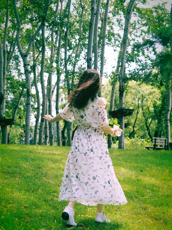 a woman in a dress stands in front of some trees