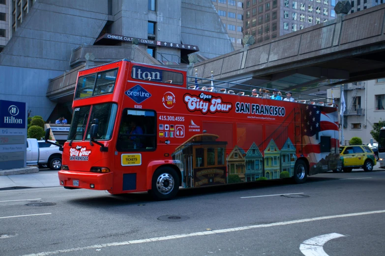 a red tour bus riding down a street with a bridge