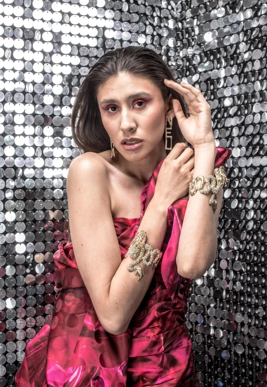 a girl with her hands in her hair, posing for a portrait with sequins on the wall behind her