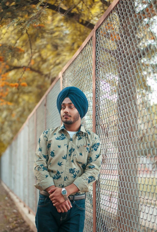 a man leaning on a fence and wearing a turban