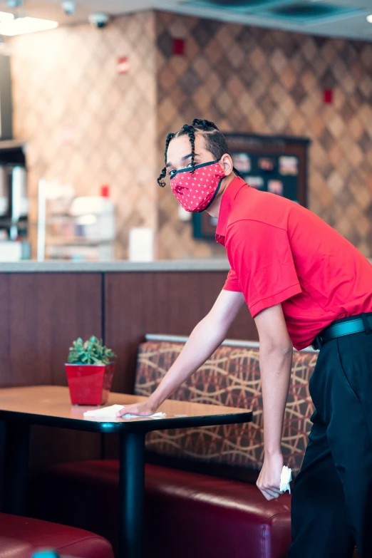 a man with red shirt and black pants wearing a face mask cleaning the table