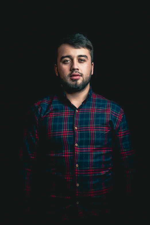 a young man standing with a beard and wearing plaid shirt