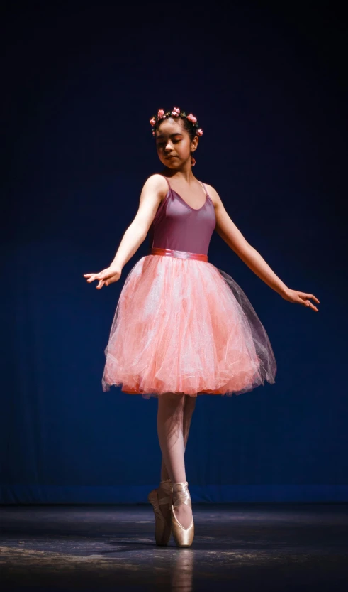 a woman in a pink tutu skirt with a tiara on, standing in front of a black backdrop