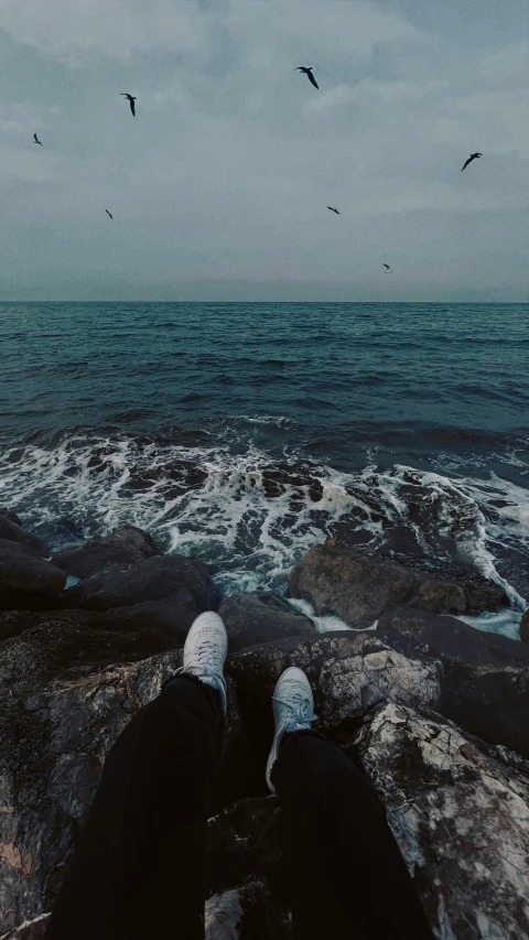 the feet and ankles of a man standing on rocks looking at the ocean