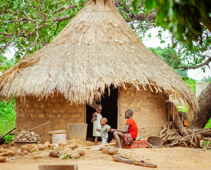 a woman and two children sit in front of a hut
