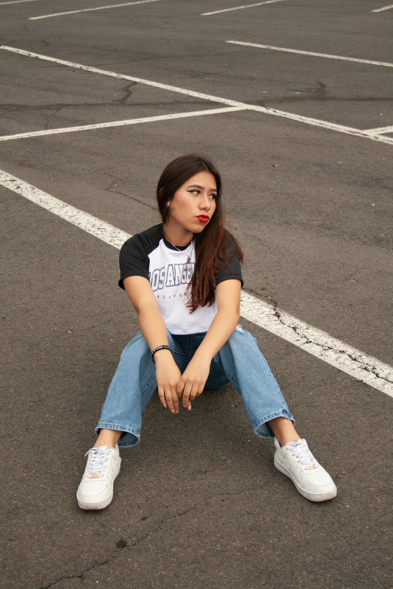 a woman sits in a parking lot wearing slip on sneakers