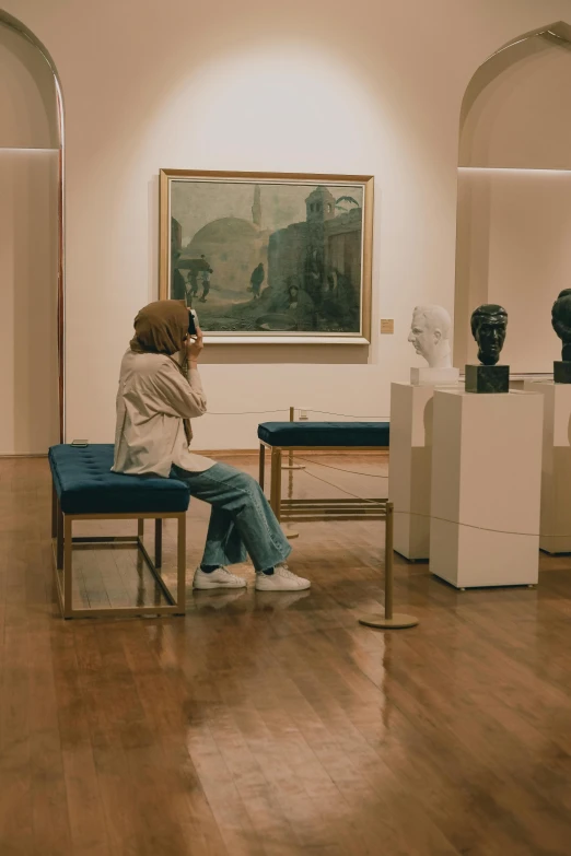 woman sitting on bench looking at sculptures in art gallery