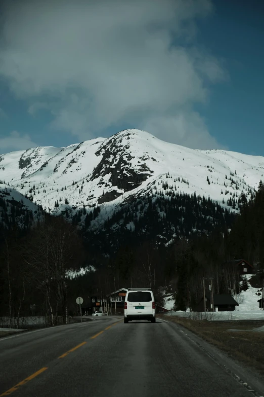 a car traveling down the road next to a snowy mountain