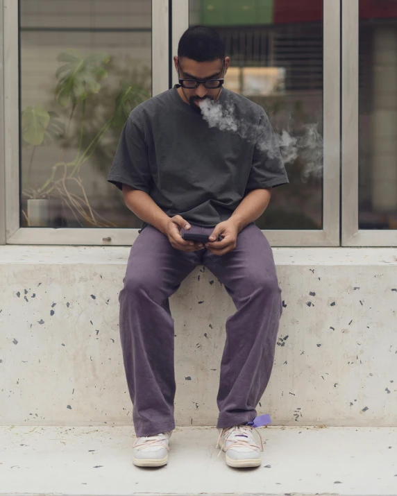 man sitting on a ledge holding his cellphone with smoke coming out of it