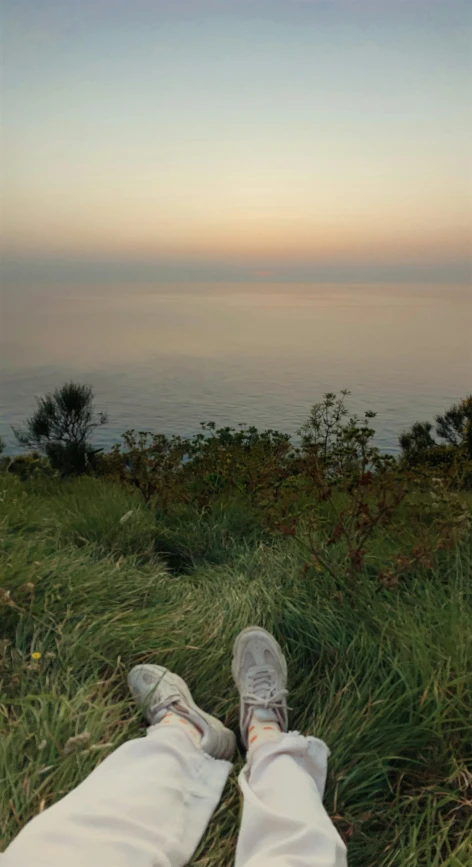 someone is sitting on the grass, overlooking the water