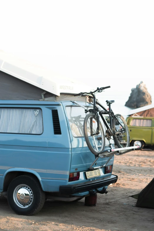 a blue van with a bike on the roof and side of it parked next to a tent