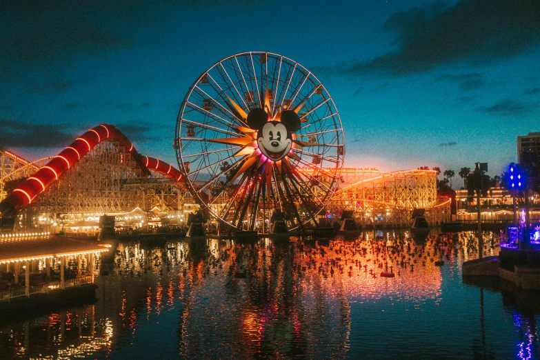 a fair with lights on it and a ferris wheel near the water