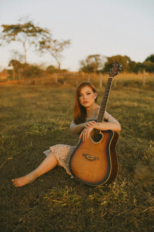 a woman is sitting in a field with her guitar