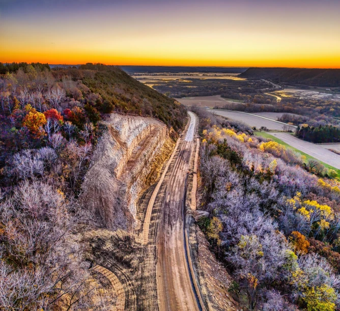 a road next to a dirt mountain with lots of trees on it