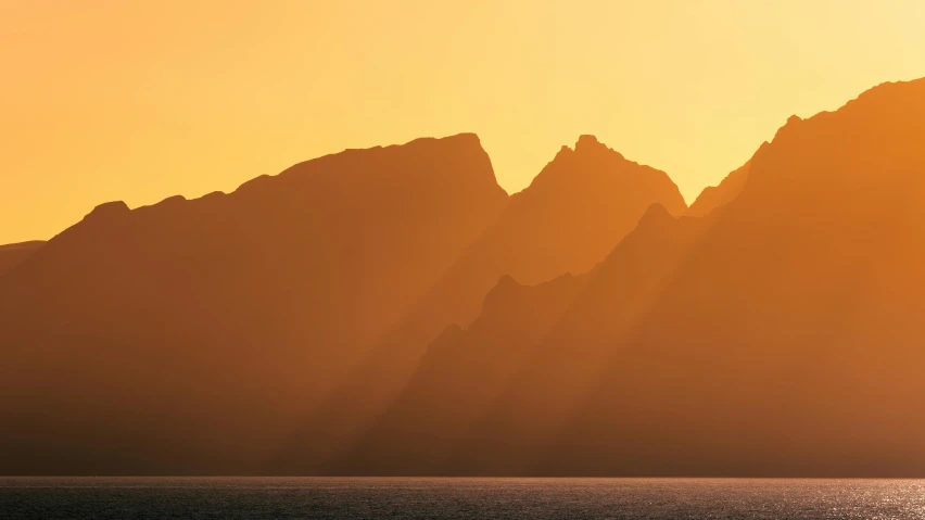 some mountains and water in front of a sunset