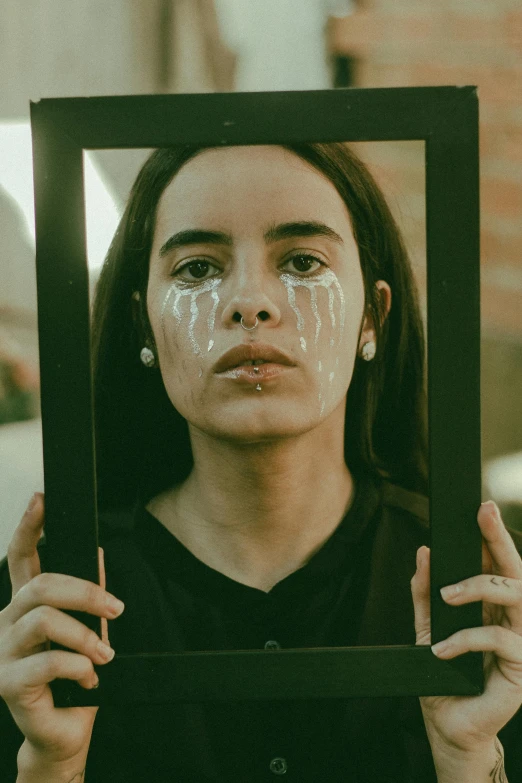 a woman with white paint on her face holding up a frame