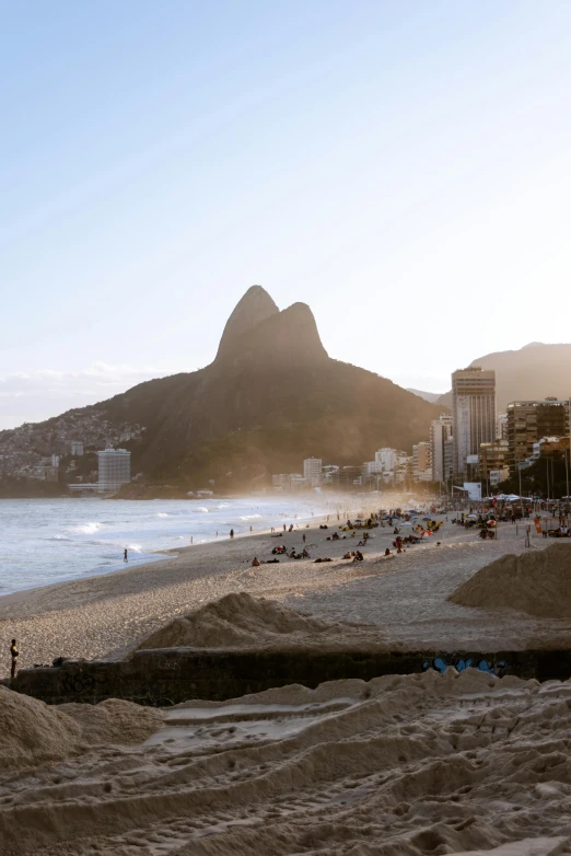 a beach area with people swimming, a mountain and buildings