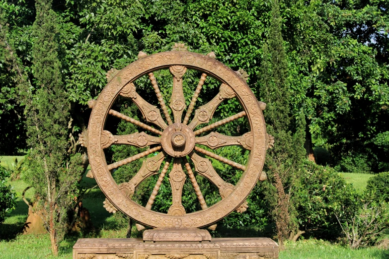 a large wheel with intricate carvings sits by the trees