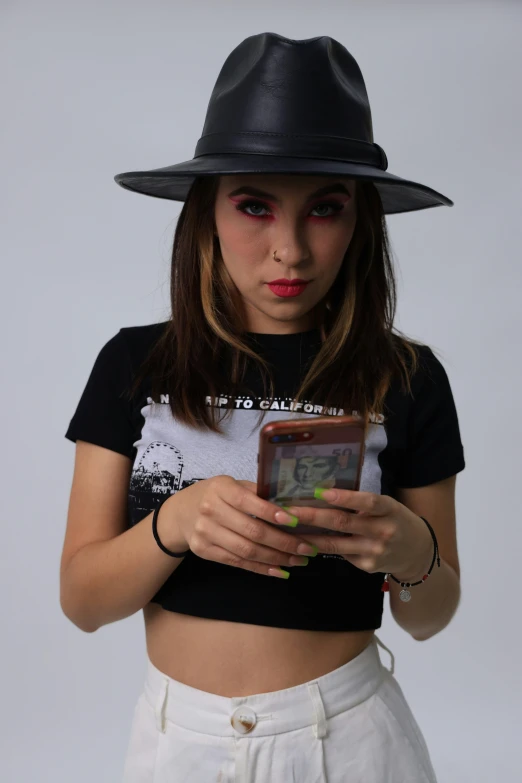 a woman with red makeup is wearing a fedora and using her phone
