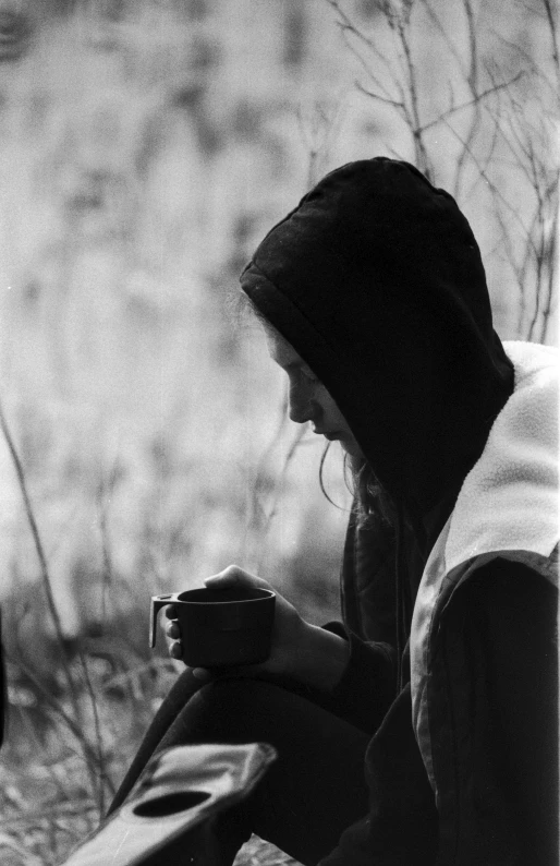 a man in a hoodie sitting on top of a bench holding a coffee cup