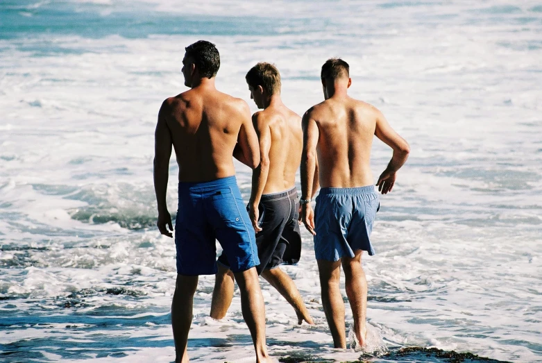 three people walking into the water at the beach