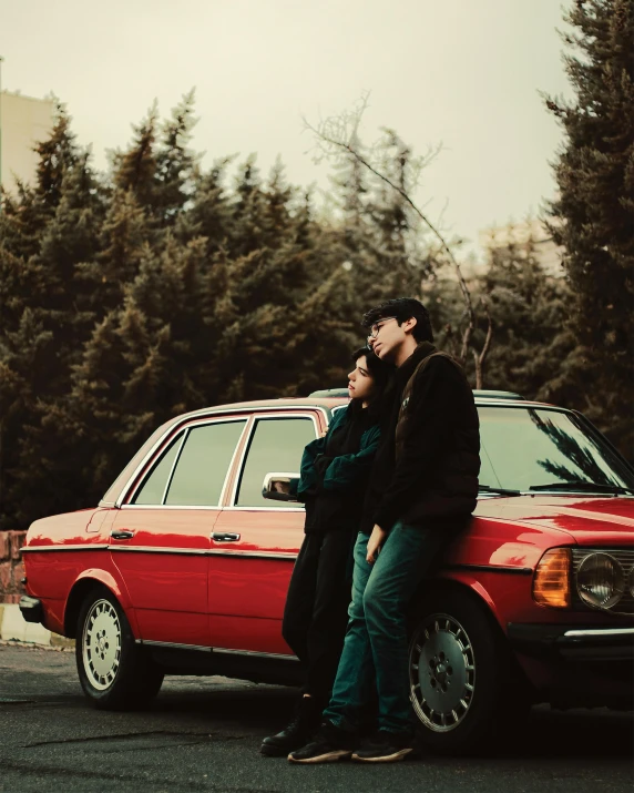 a couple standing next to a red car in the driveway