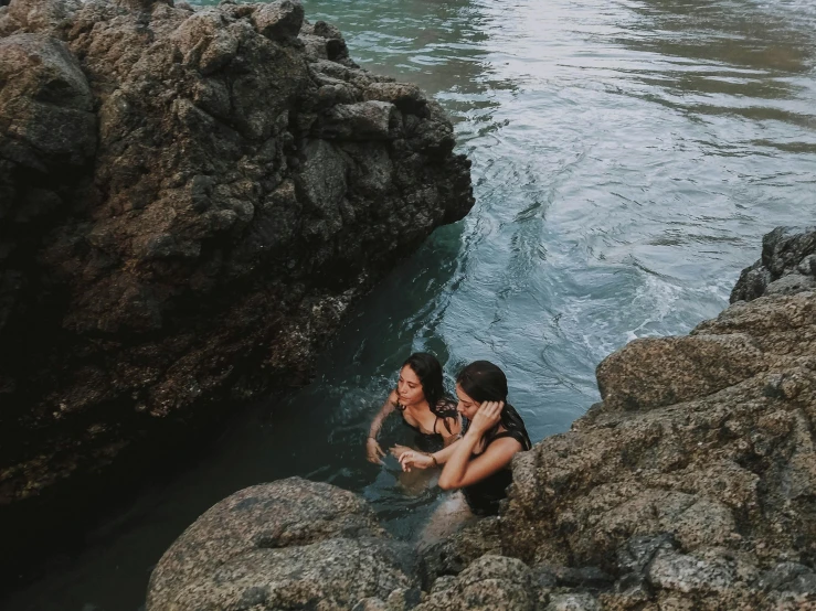 two women, one sitting on rocks, emcing in the water