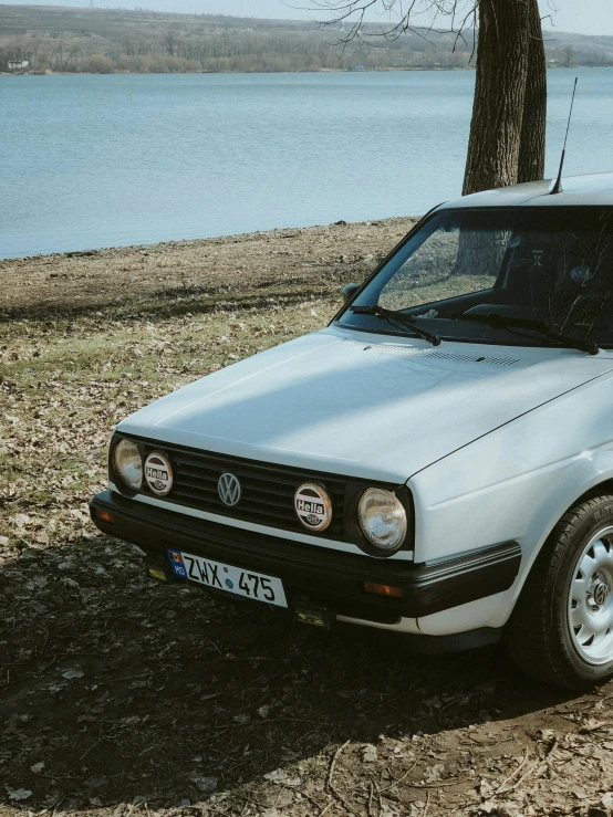 a small white car parked next to water and tree