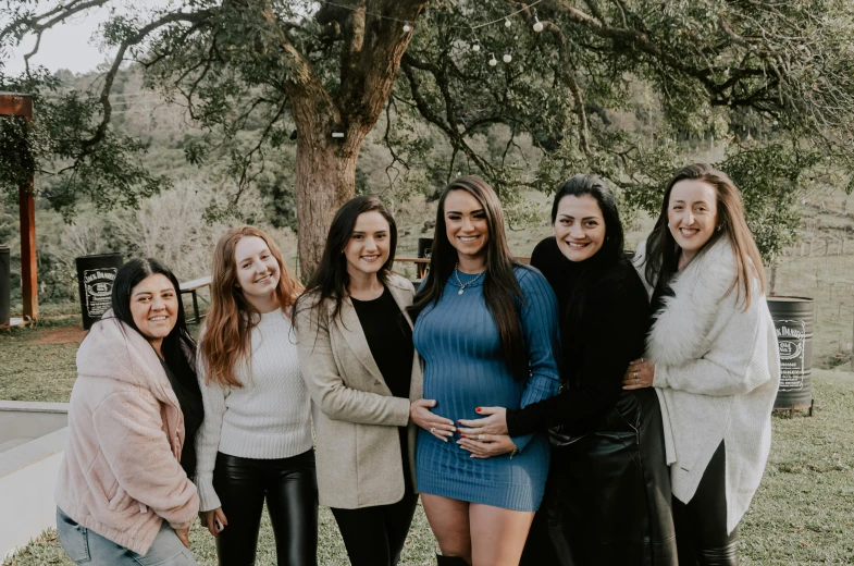 a group of women stand in front of a tree