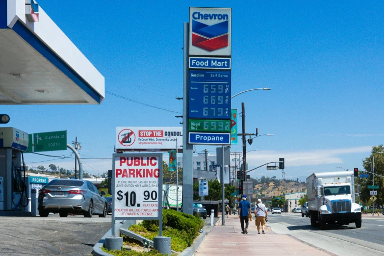 the people are walking along the sidewalk near a gas station