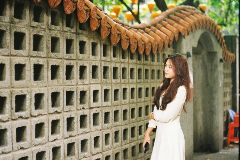 woman with long hair wearing white dress next to brick wall