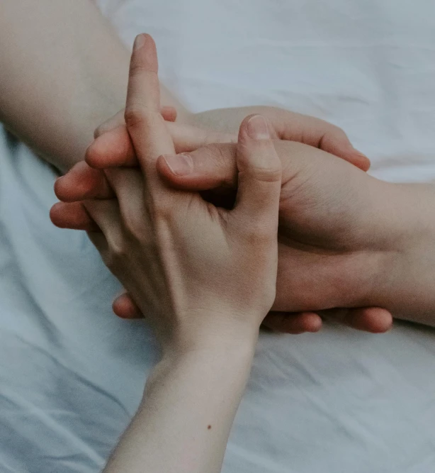 two hands reaching each other together on a white bed