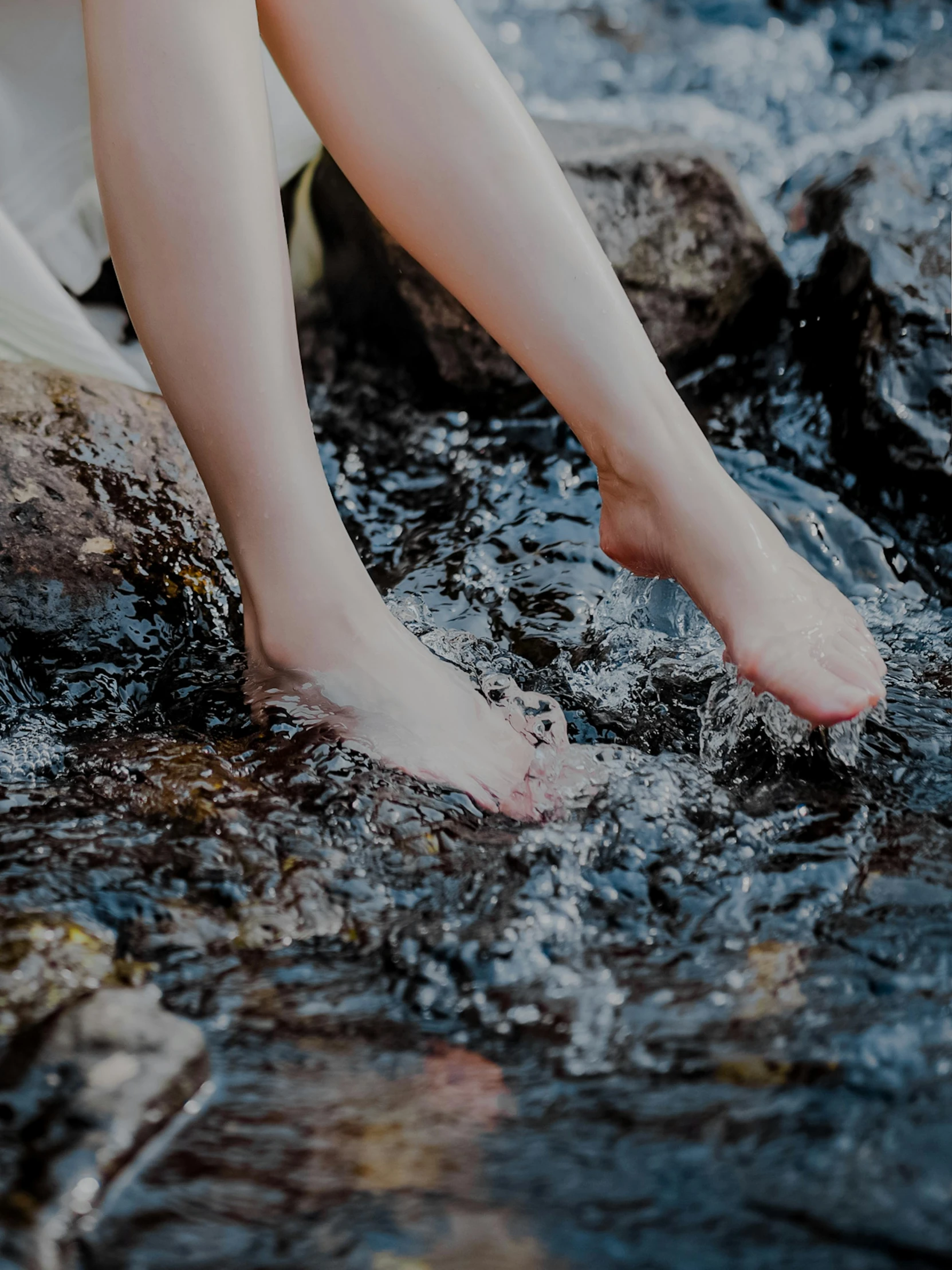 barefoot woman sitting on a rock near a stream