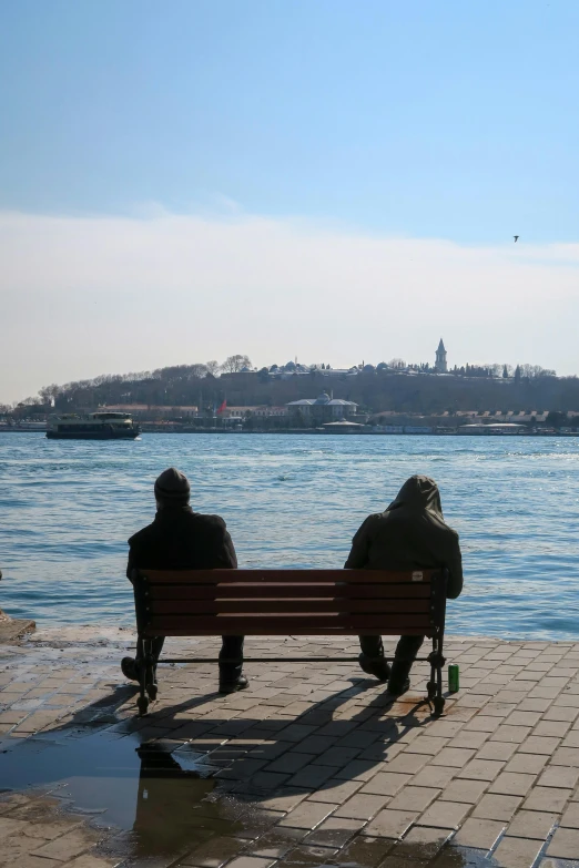 two people sit on a bench in front of a body of water