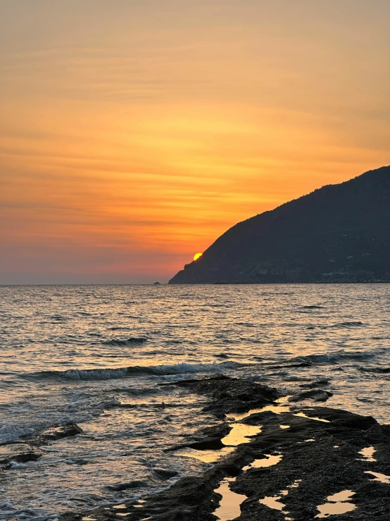 the sun is setting over the water and rocks