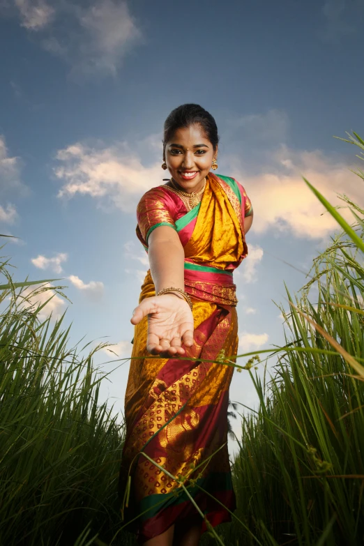 a woman in a colorful sari is standing by tall grass