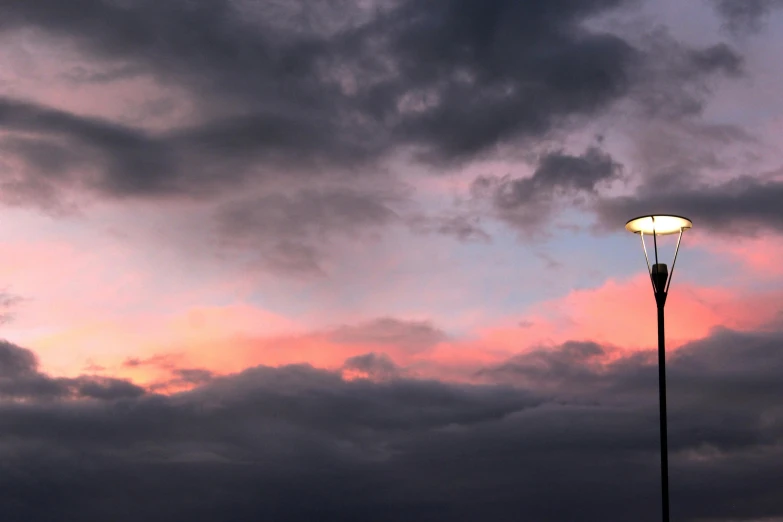 the clouds are moving down as a streetlight sits against the dusk sky