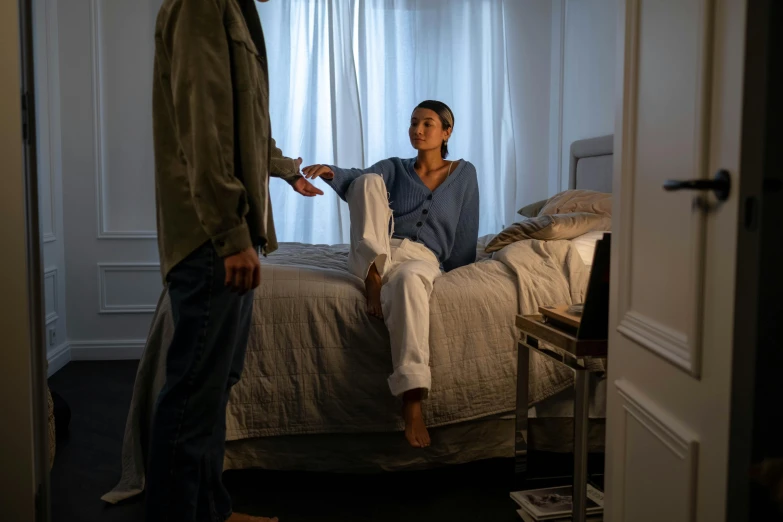 a woman sitting on a bed and an man standing by her