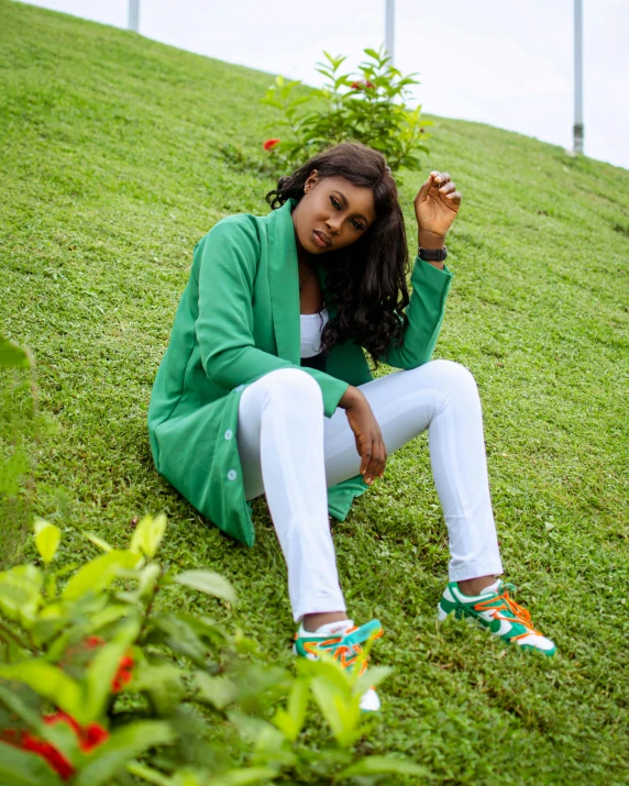 a young woman sitting on a grassy hill, in front of some trees