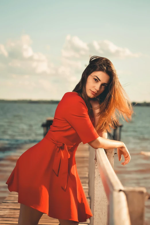 a woman poses on a pier in front of the water